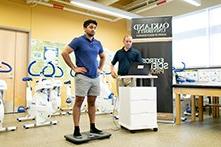 Man standing on an electronic device in an exercise science classroom with fitness equipment.